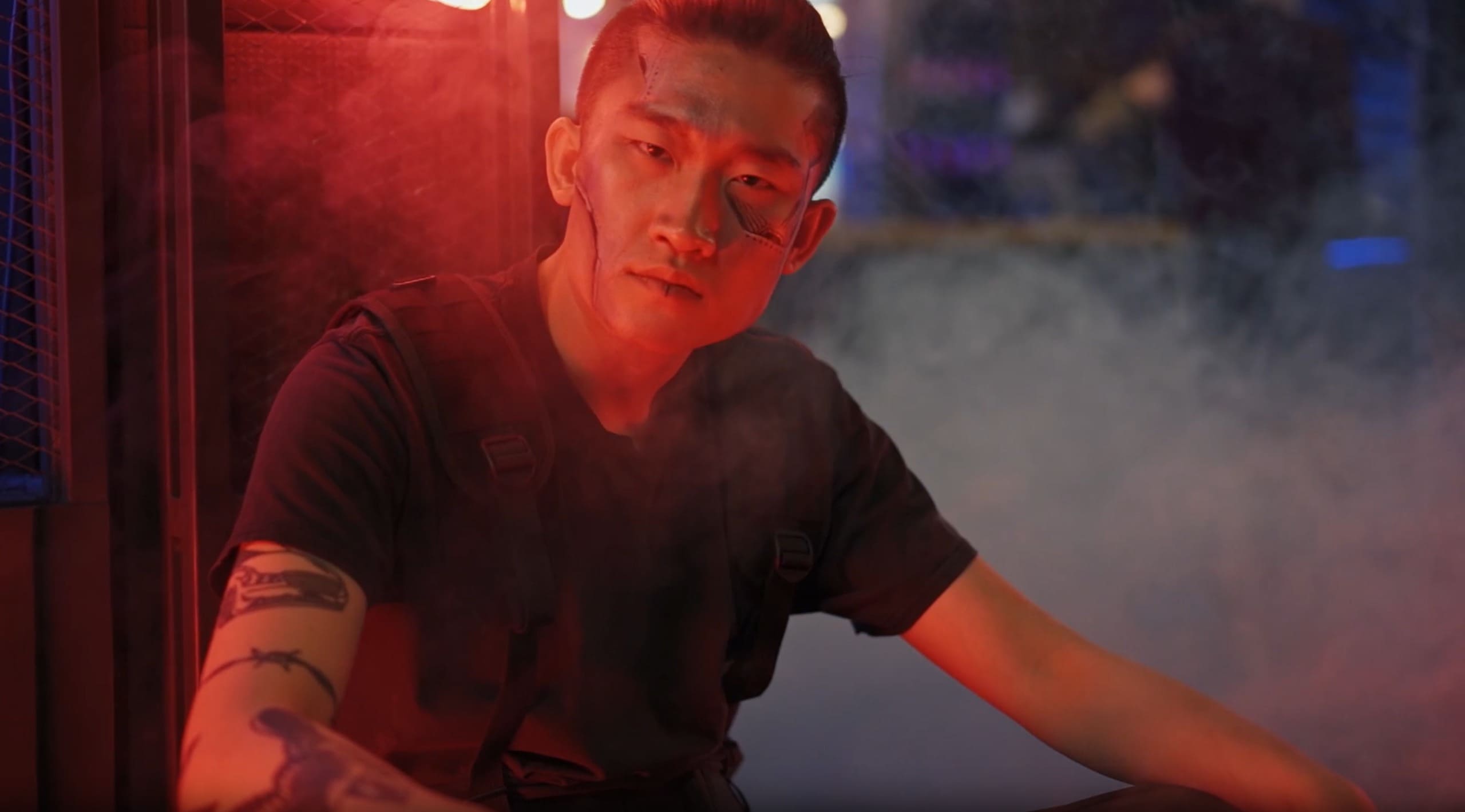 Tattooed portrait lit in red and smoke against a cage backdrop