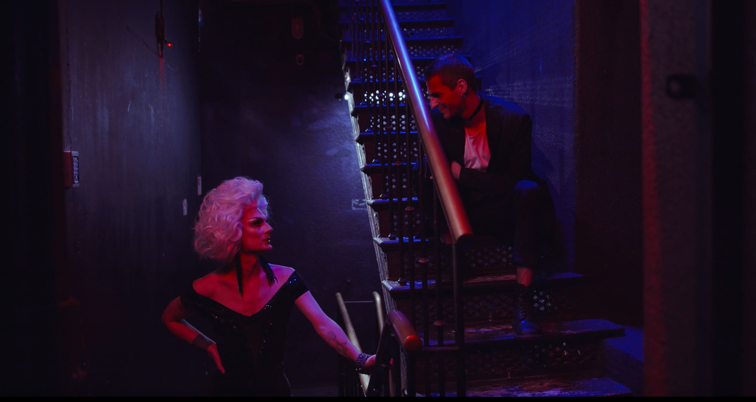 A performer and a patron on the staircase, lit in moody color